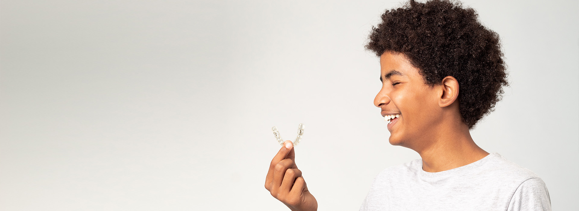 Teen smiling while holding Invisalign clear aligner