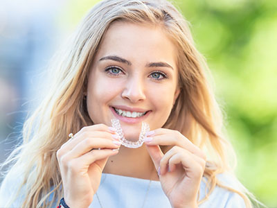 Teen girl smiling while holding Invisalign clear aligner